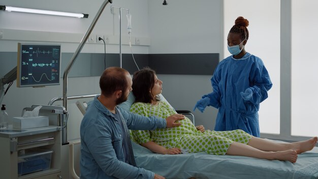병원에서 출산 병동에서 아기를 기대하는 백인 부부. 침대에 앉아 아프리카계 미국인 간호사와 젊은 남편과 이야기하는 임신한 여자. 출산 의료 지원