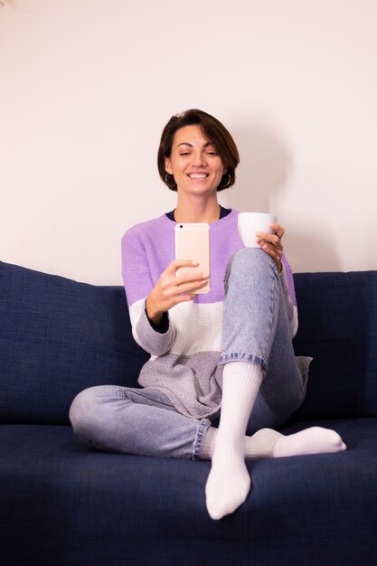 暖かい紫色のセーターのプルオーバーで自宅で白人のかわいい女性ブロガーは、携帯電話の鏡で自分撮りを取ります