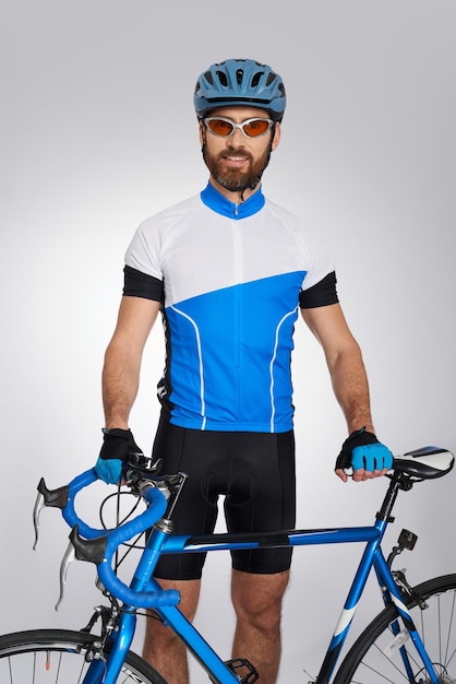 Caucasian cyclist in full gear posing with bike in studio portrait of smiling darkhaired athlete in