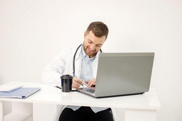 Caucasian doctor sitting at workplace and using laptop