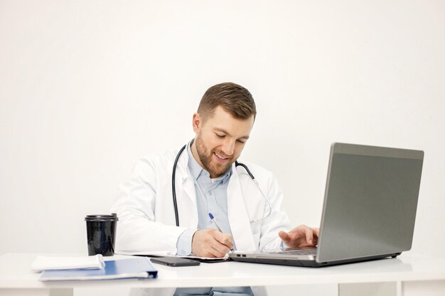 Кавказский врач сидит на рабочем месте и пользуется ноутбуком