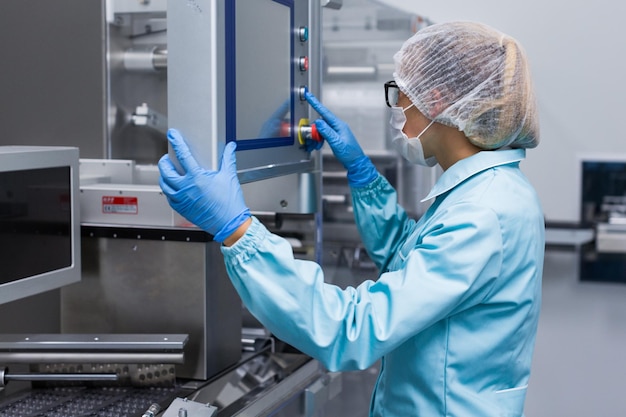 Caucasian factory worker in blue lab suit configures machine look at control panel