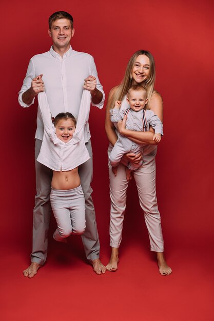 Caucasian family with two children poses for the camera together, picture isolated on red background