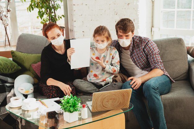 Caucasian famiy in face masks and gloves isolated at home with coronavirus respiratory symptoms such as fever, headache, cough in mild condition. Healthcare, medicine, quarantine, treatment concept.