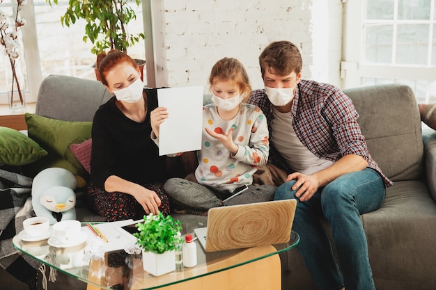 Caucasian famiy in face masks and gloves isolated at home with coronavirus respiratory symptoms such as fever, headache, cough in mild condition. Healthcare, medicine, quarantine, treatment concept.