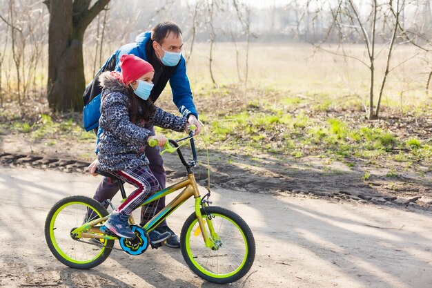 백인 아버지는 pm2.5와 코로나바이러스 코비드-19 팬데믹 바이러스 증상을 보호하기 위해 보호 마스크를 쓰고 딸이 자전거를 타는 것을 돕습니다.