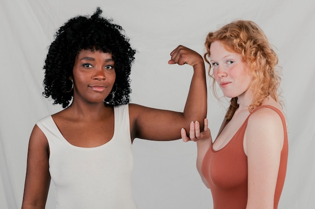 Free photo caucasian female holding the hand of an african young woman flexing her muscle
