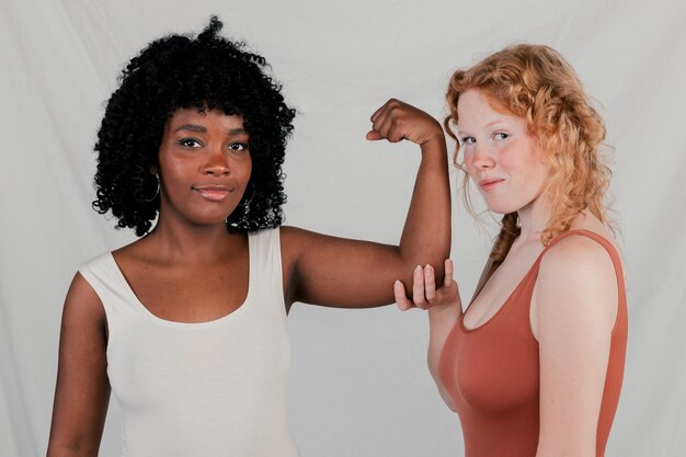 Caucasian female holding the hand of an african young woman flexing her muscle