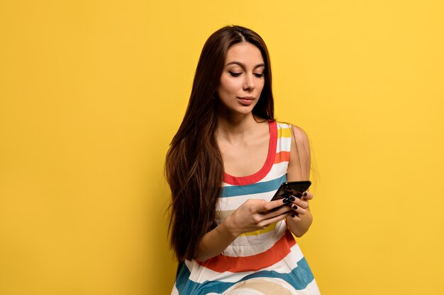 Caucasian female university student wearing brightful dress looking at smartphone smiling happy