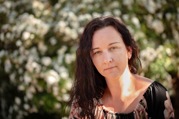 Caucasian female wearing a floral dress sitting in front of a wall of white flowers