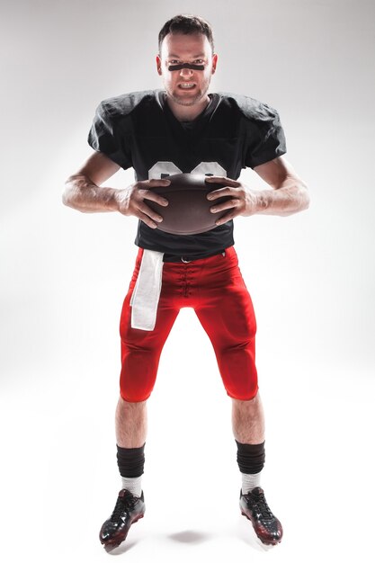 Caucasian fitness man as american football player holding a ball on white background