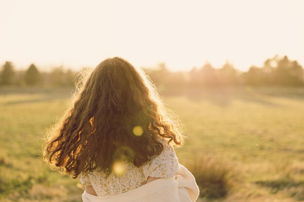 Caucasian girl from behind standing in a field on a sunny day concept of happiness