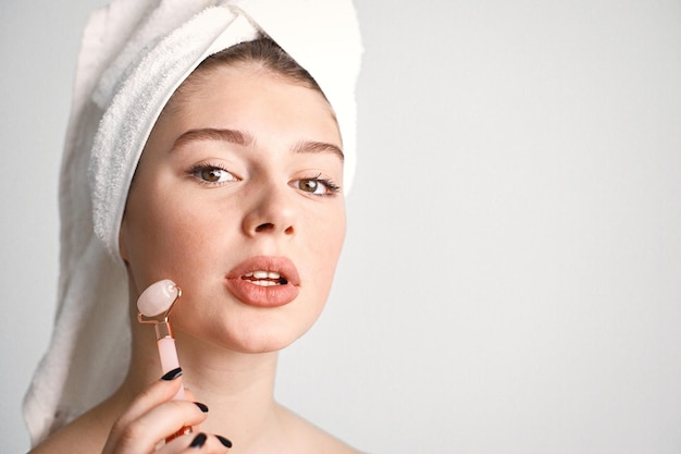 Caucasian girl with towel on a head using jade roller isolated on white background