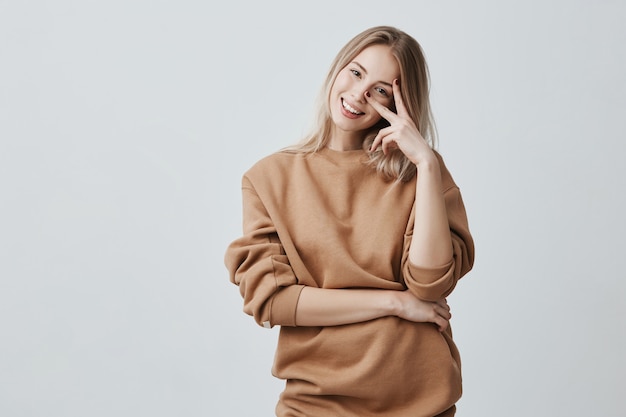 Caucasian good-looking attractive young female with long blonde hair dressed in casual clothes, smiling broadly during interesting conversation. Young woman expressing positive emotions