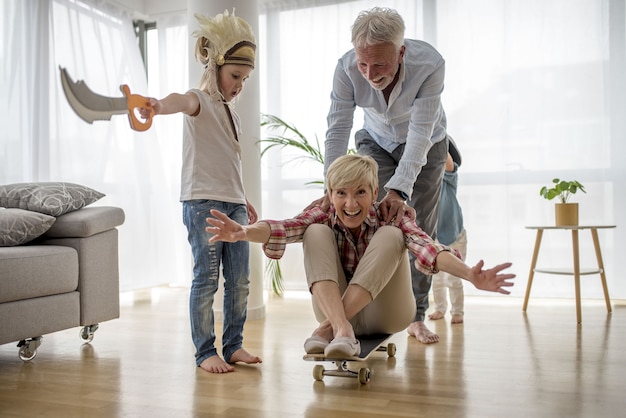 Caucasian grandfather pushing grandmother  on skateboard inside with grandson wearing pirate costume
