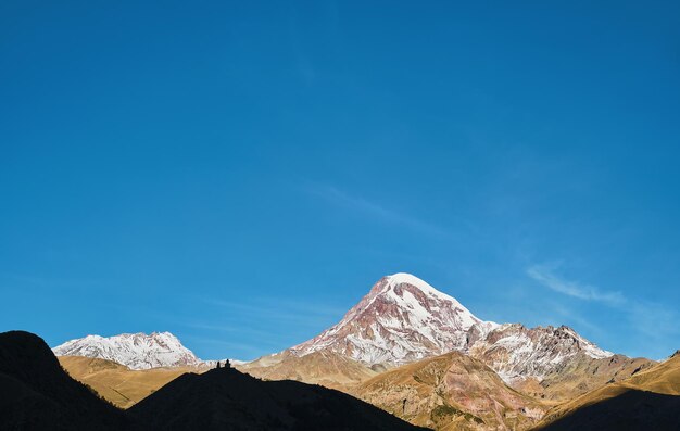 コーカサス地方の高地、昇る太陽に照らされたカズベク山の頂上、初秋、ジョージア州の旅行と観光、山でのトレッキング