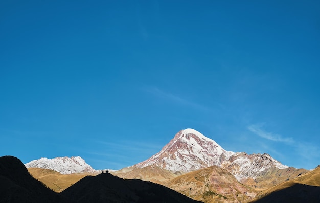 コーカサス地方の高地、昇る太陽に照らされたカズベク山の頂上、初秋、ジョージア州の旅行と観光、山でのトレッキング