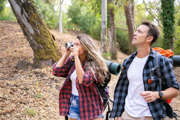 백인 등산객 사진 촬영, 산책 또는 나무로 둘러싸인 숲길 트레킹. 예쁜 여자 카메라를 들고, 촬영 및 잘 생긴 남자와 하이킹. 관광, 모험 및 휴가 개념
