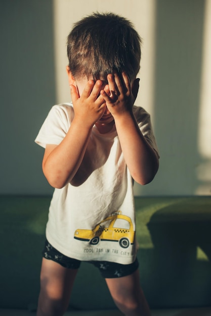Caucasian kid hiding his face behind palms of his hands front view Premium Photo