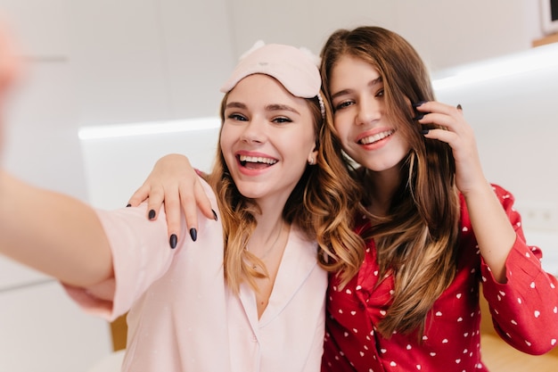 Caucasian laughing lady making selfie with friend in good weekend morning. Refined girl with long hairstyle having fun with cute sister.