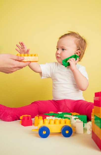 Caucasian little girl, children isolated on yellow studio background. Portrait of cute and adorable kid, baby playing and looks serious.