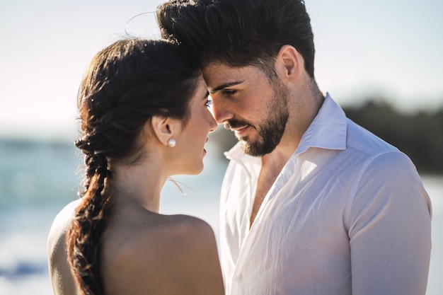 Coppie amorose caucasiche che indossano vestiti bianchi e che abbracciano in spiaggia durante un servizio fotografico di matrimonio