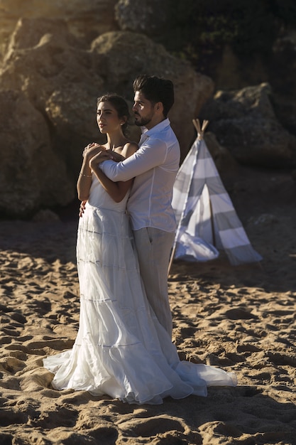 白い服を着て、結婚式の写真撮影中にビーチで抱き締める白人の愛情のあるカップル