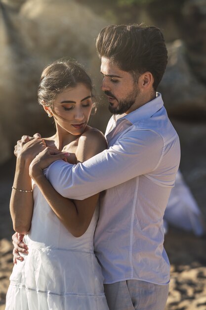Кавказская влюбленная пара в белой одежде и обниматься на пляже во время свадебной фотосессии