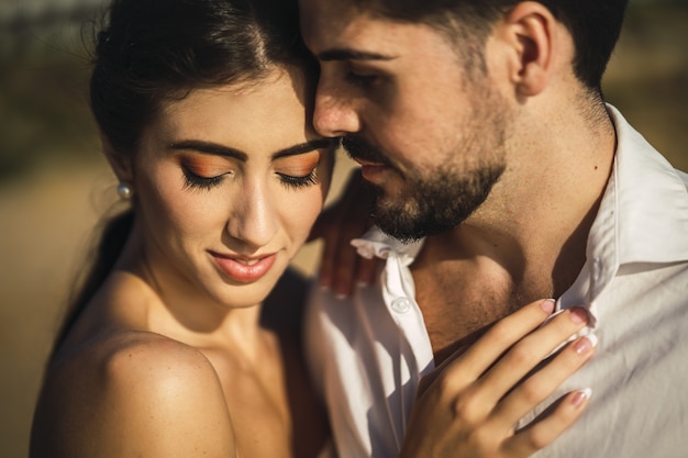 Caucasian loving couple wearing white clothes and hugging in the beach during a wedding photoshoot