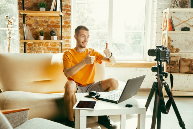 Caucasian male blogger with camera recording video review of gadgets at home