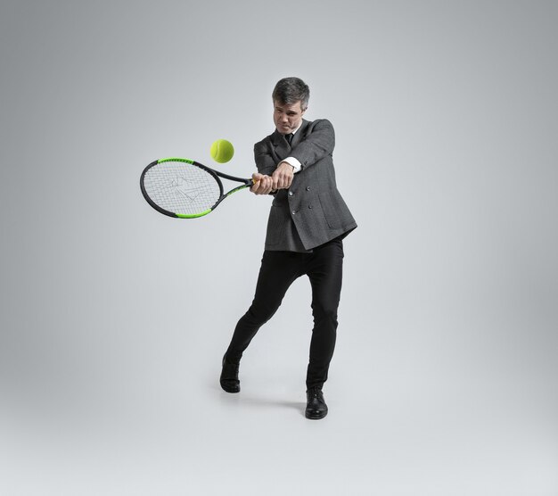 Кавказский мужчина в офисной одежде играет в теннис на серой стене