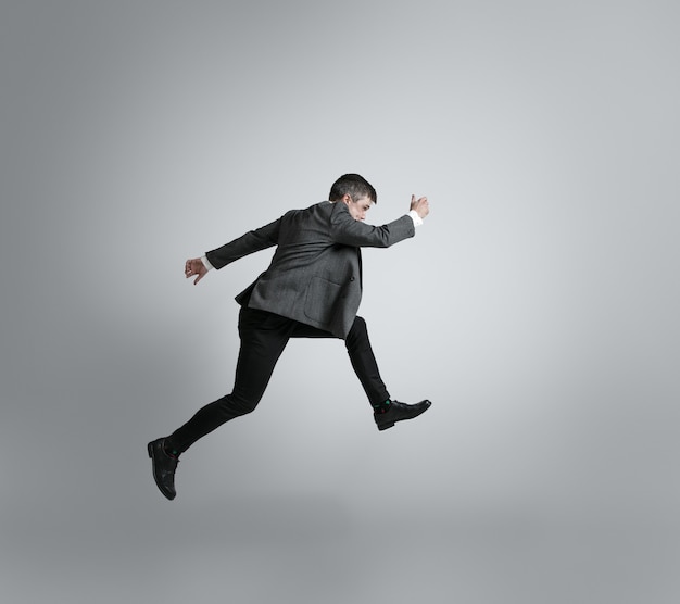 Free photo caucasian man in office clothes running isolated on grey  wall