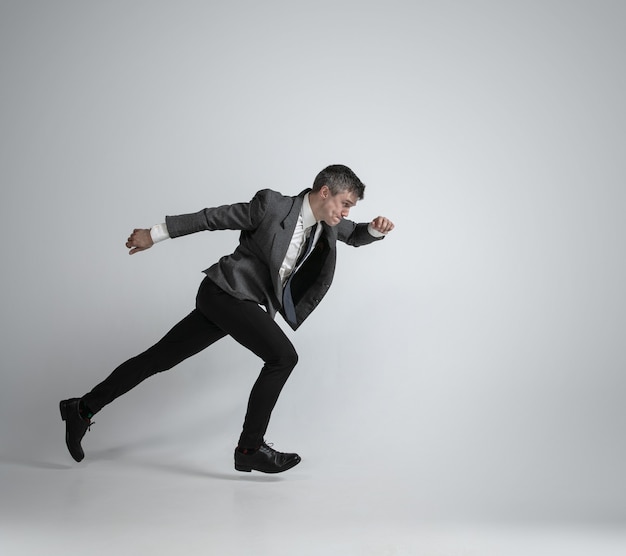 Caucasian man in office clothes running like a professional sportsman on grey background.