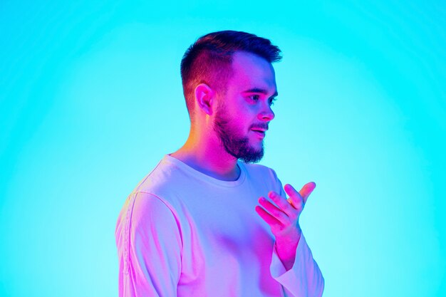 Caucasian man's portrait isolated on blue studio background in neon light. Beautiful male model. Concept of human emotions, facial expression, sales, ad. Copyspace for ad.
