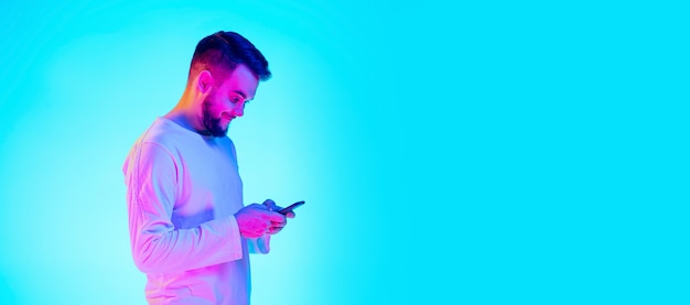 Caucasian man's portrait isolated on blue studio background in neon light. Beautiful male model. Concept of human emotions, facial expression, sales, ad. Copyspace for ad.