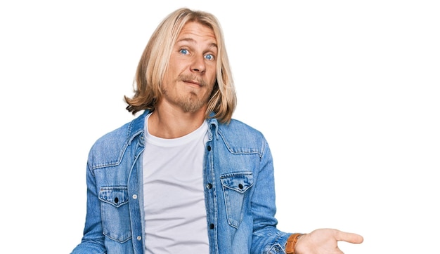 Free photo caucasian man with blond long hair wearing casual denim jacket clueless and confused with open arms, no idea concept.