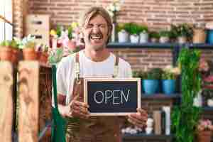 Free photo caucasian man with mustache working at florist holding open sign smiling and laughing hard out loud because funny crazy joke.