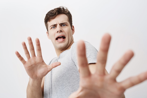 Caucasian man with scared expression on his face making frightened gesture with his palms as if trying to defend himself. Fearful european young male asking to stop, gesturing with his hands