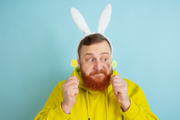 Free photo caucasian man with traditional decor as an easter bunny with bright casual clothes on blue studio background.