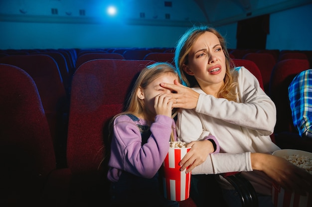 映画館、家または映画館で映画を見ている白人の母と娘。