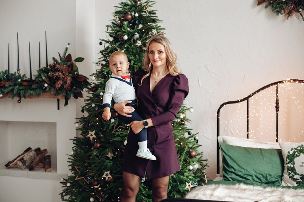 Caucasian mother holds her lovely daughter on the hands near the christmas tree at home