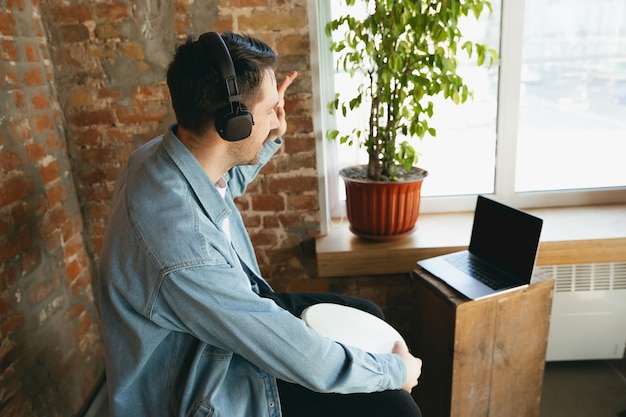 Musicista caucasico che suona il tamburo a mano durante il concerto online a casa isolato e messo in quarantena.