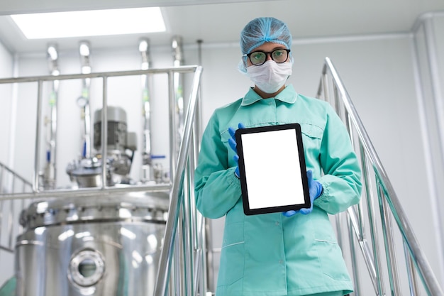 Free photo caucasian scientist in blue lab uniform stand on chromed stairs and hold empty tablet towards camera