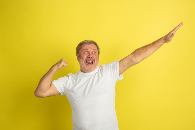 Caucasian senior man's portrait isolated on yellow studio wall