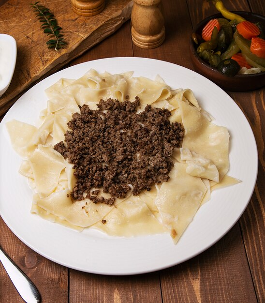 Caucasian traditional foor khingal, khinkali. Caucasian pasta with meat in white plate on wooden table.