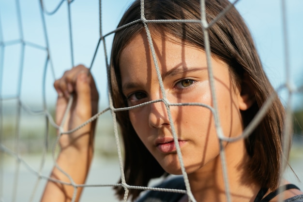 Foto gratuita adolescente bianco caucasico in posa dietro una rete su un campo sportivo