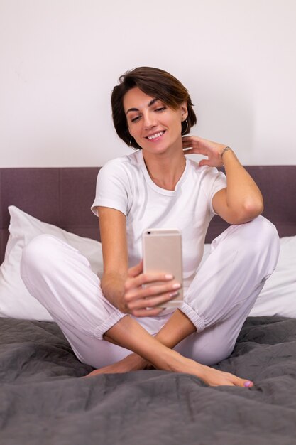 Caucasian woman blogger at home in casual clothes cozy bedroom take photo selfie on mobile phone in mirror