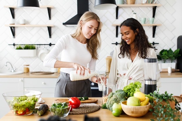 Free photo caucasian woman is pouring milk in a glass and african woman stands near