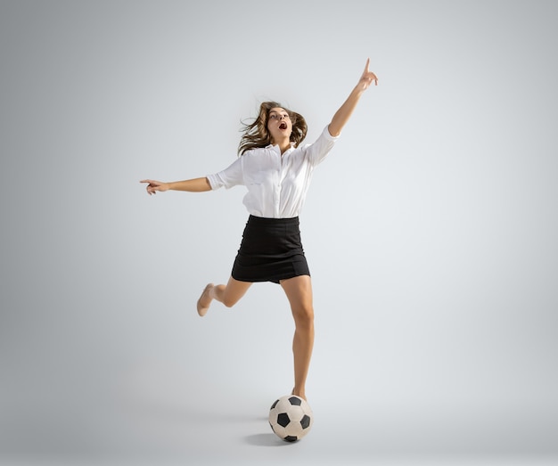 Caucasian woman in office clothes kicking ball isolated on grey wall
