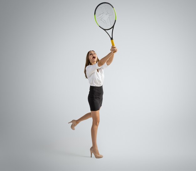 Caucasian woman in office clothes plays tennis on grey